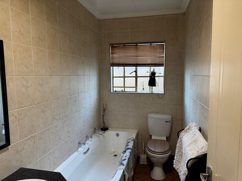 A functional bathroom featuring a built-in bathtub, toilet, and neutral wall tiling, offering a dated aesthetic ready for modernization.