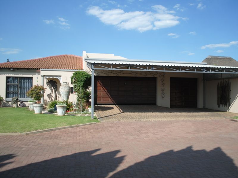 Front elevation of a residential property featuring a double garage, attached carport, paved driveway, and well-maintained garden area.