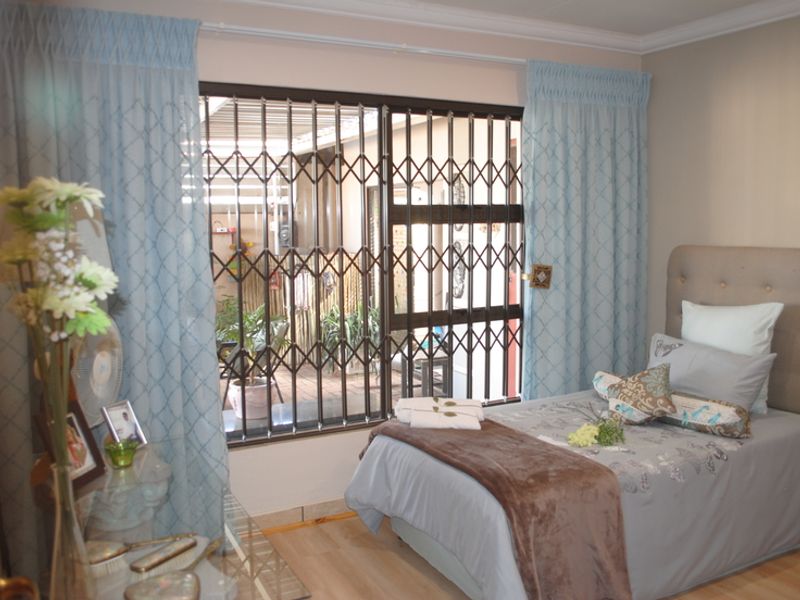 A bedroom featuring laminate flooring and a sliding glass door with a security gate, providing direct access to an outdoor patio area.