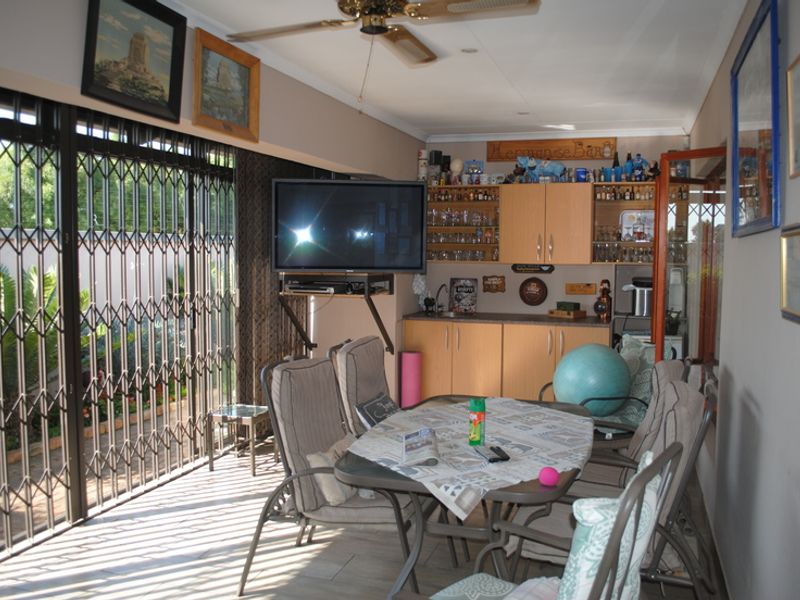 A covered patio area featuring built-in bar cabinetry with a sink, ceiling fan, and secure metal sliding doors leading to the garden.