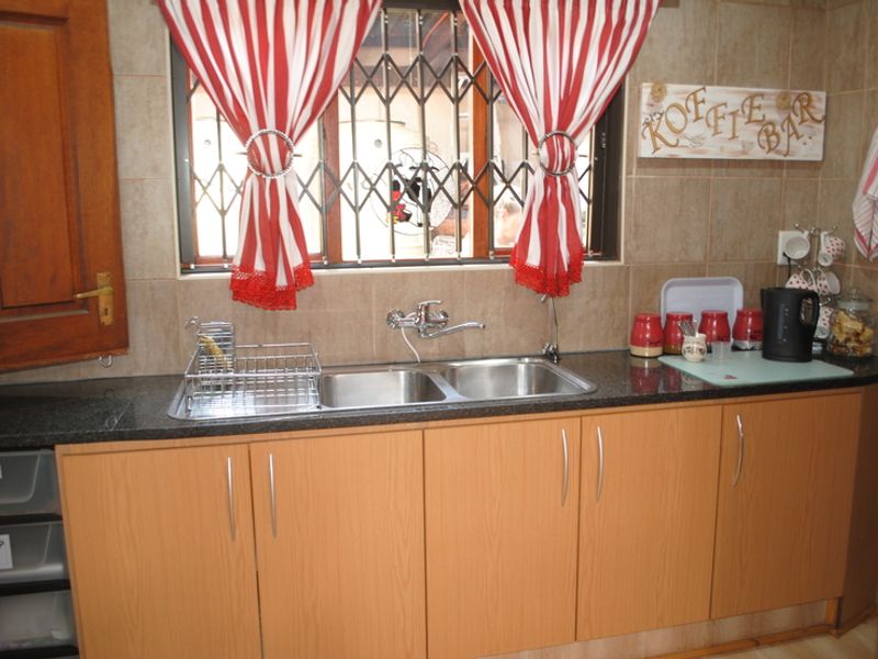 A functional kitchen area featuring laminate cabinetry, granite countertops, a double bowl stainless steel sink, and a tiled backsplash with a security gate window.