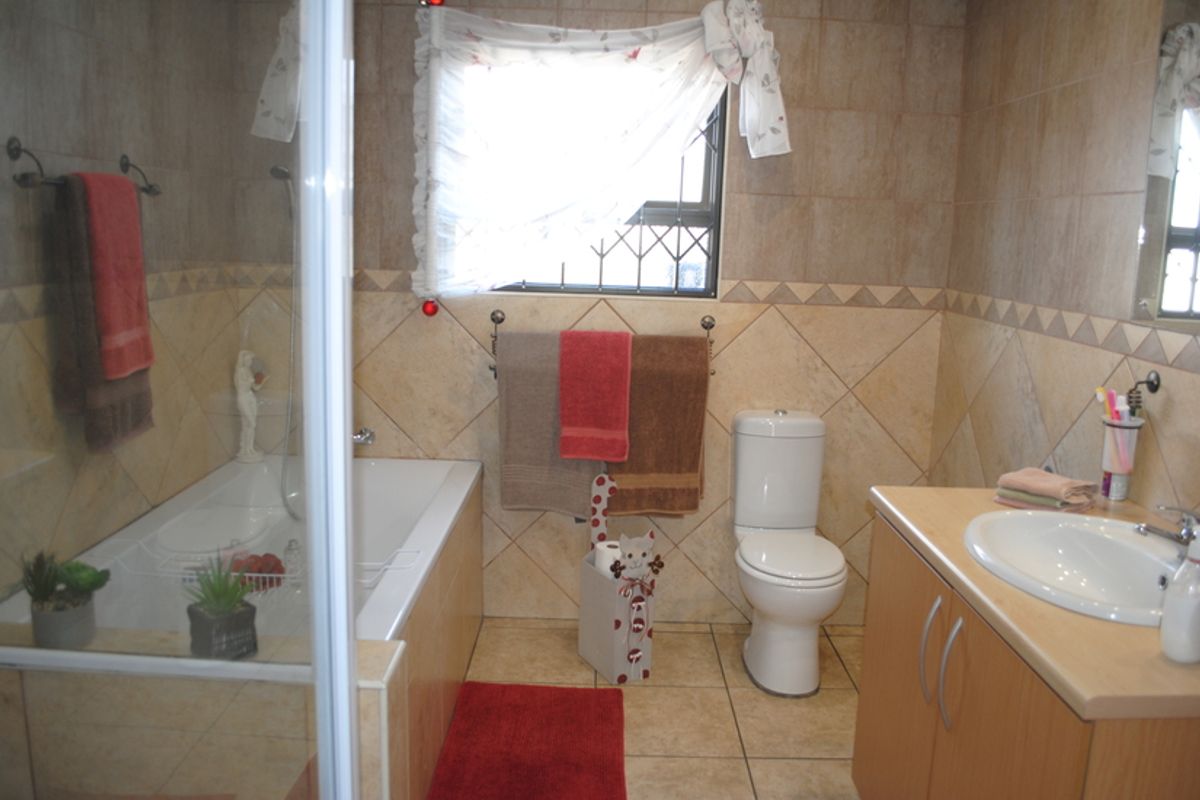 A functional bathroom featuring a bathtub, separate shower enclosure, toilet, and a vanity cabinet with a washbasin, finished with neutral wall and floor tiles.