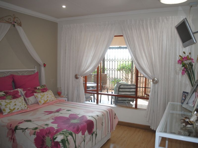 A bedroom featuring laminate flooring, recessed lighting, and a sliding glass door with an integrated security gate leading to an outdoor area.