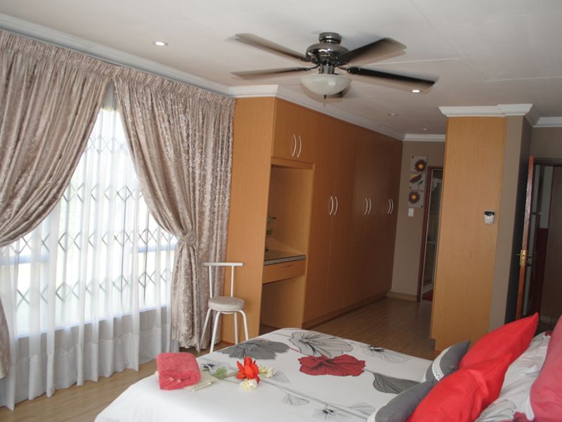 A well-maintained bedroom featuring extensive built-in wooden cabinetry, laminate flooring, a ceiling fan, and large windows with security gates.