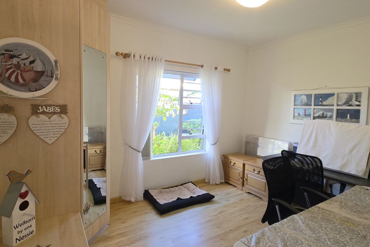A bedroom featuring laminate flooring, a built-in wardrobe with a mirror, and a window allowing natural light.