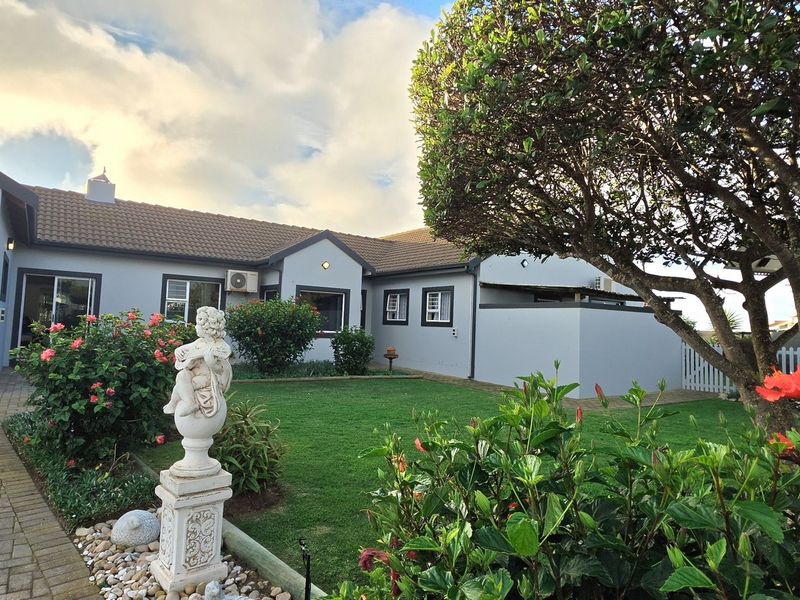 Front view of a well-maintained house featuring a paved driveway, garage, and landscaped garden area with established trees and shrubs.
