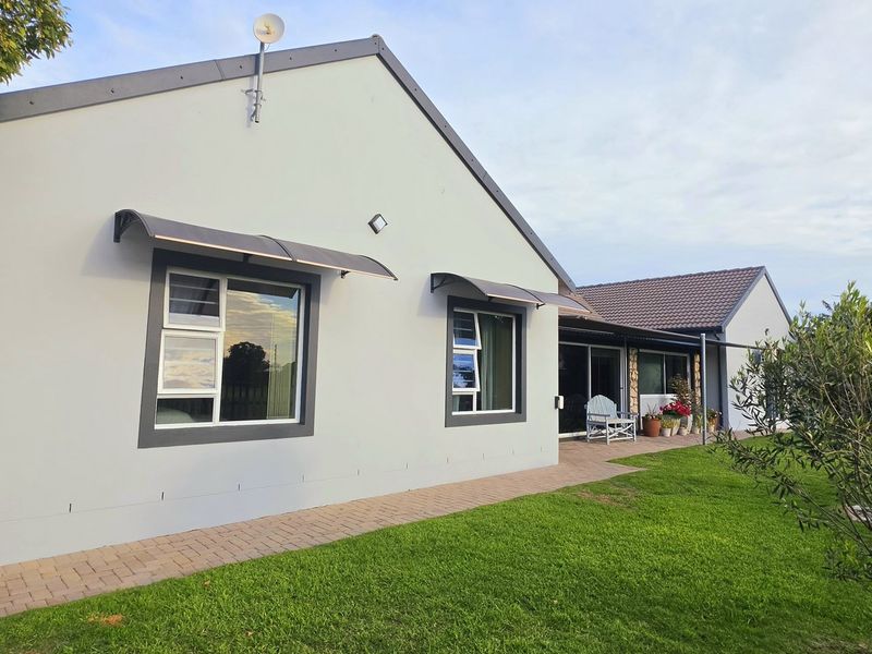 Rear view of the house featuring a paved walkway, well-maintained lawn, and modern exterior finishes with installed awnings and sliding glass doors.