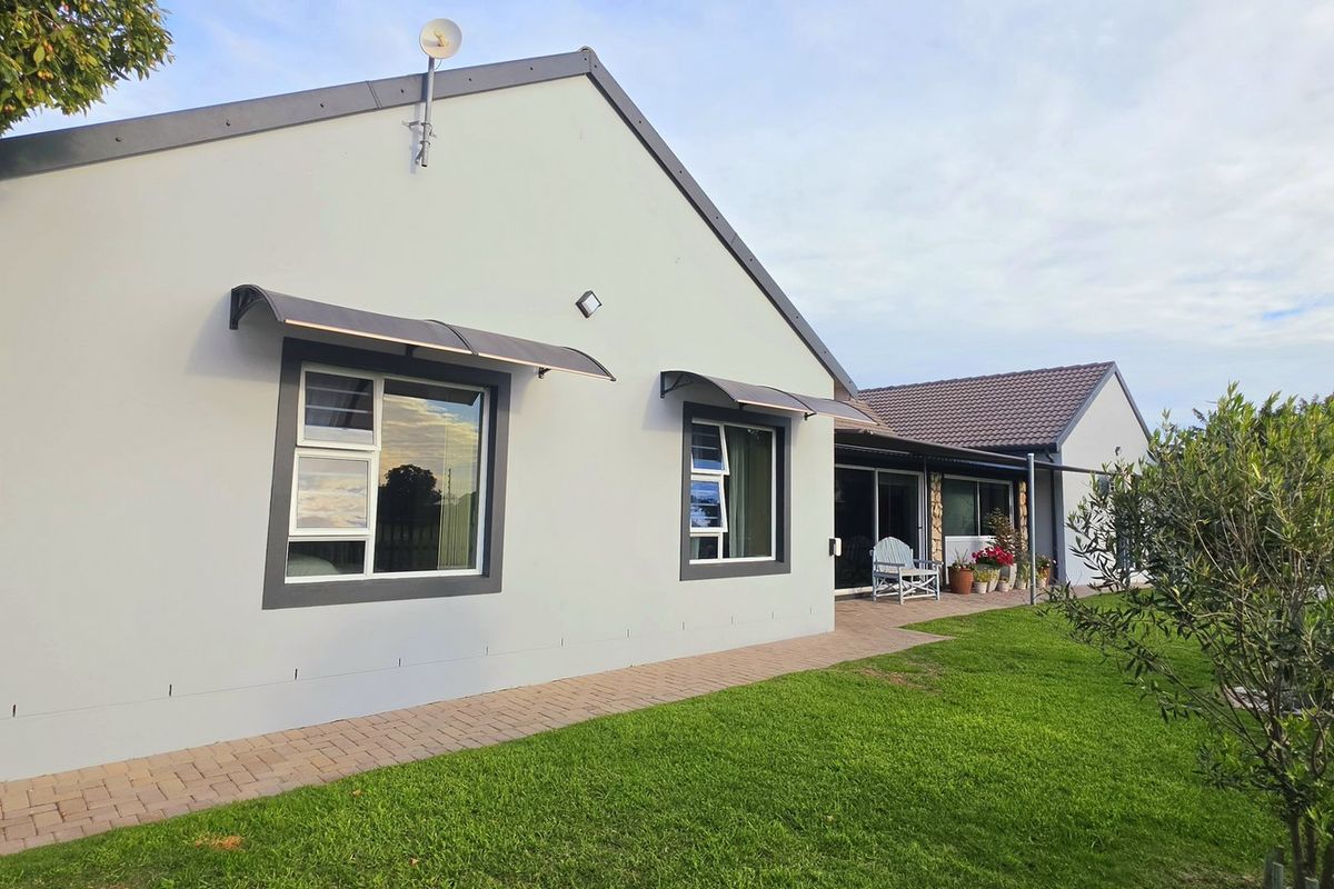 Rear view of the house featuring a paved walkway, well-maintained lawn, and modern exterior finishes with installed awnings and sliding glass doors.