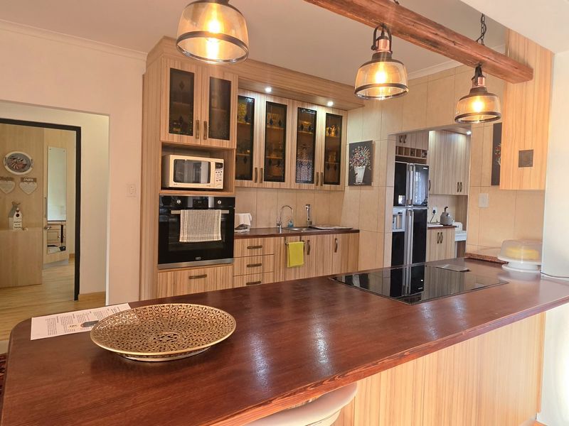 A well-maintained kitchen featuring timber cabinetry, a large breakfast bar with an integrated cooktop, built-in oven, and modern pendant lighting.