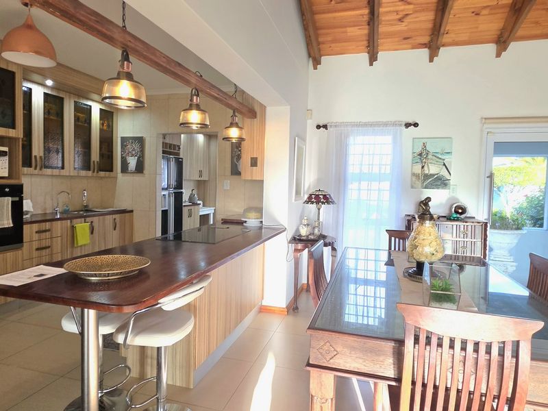 Open-plan kitchen and dining area featuring timber cabinetry, a breakfast bar, exposed ceiling beams, and direct access to an outdoor patio.