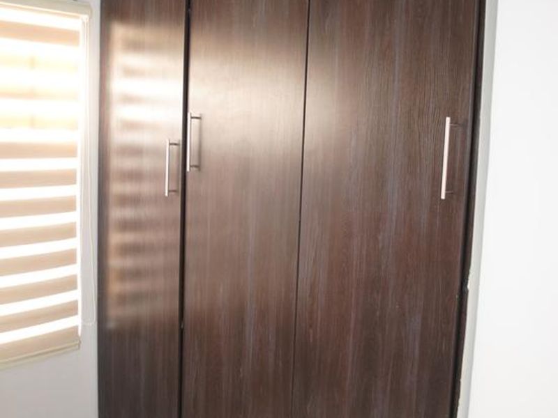A bedroom featuring dark wood-finish built-in cupboards, neutral tiled flooring, and modern roller blinds.