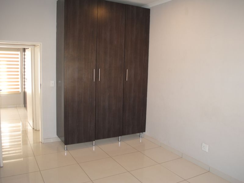 A clean, empty bedroom featuring neutral tiled flooring and a large, dark wood-finish built-in wardrobe.