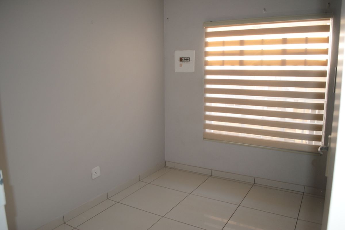 A clean, empty bedroom featuring neutral tiled flooring, light grey walls, and modern zebra blinds, providing a versatile space ready for personalization.
