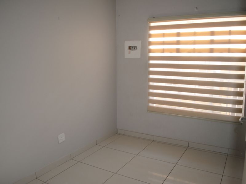 A clean, empty bedroom featuring neutral tiled flooring, light grey walls, and modern zebra blinds, providing a versatile space ready for personalization.