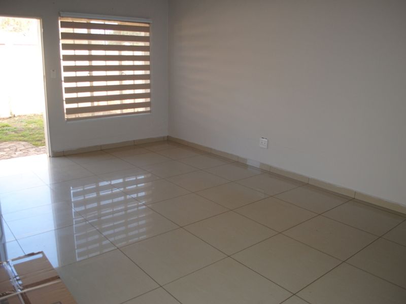 A bright, empty living room featuring neutral tiled flooring, clean walls, and modern zebra blinds with direct access to the outdoor area.