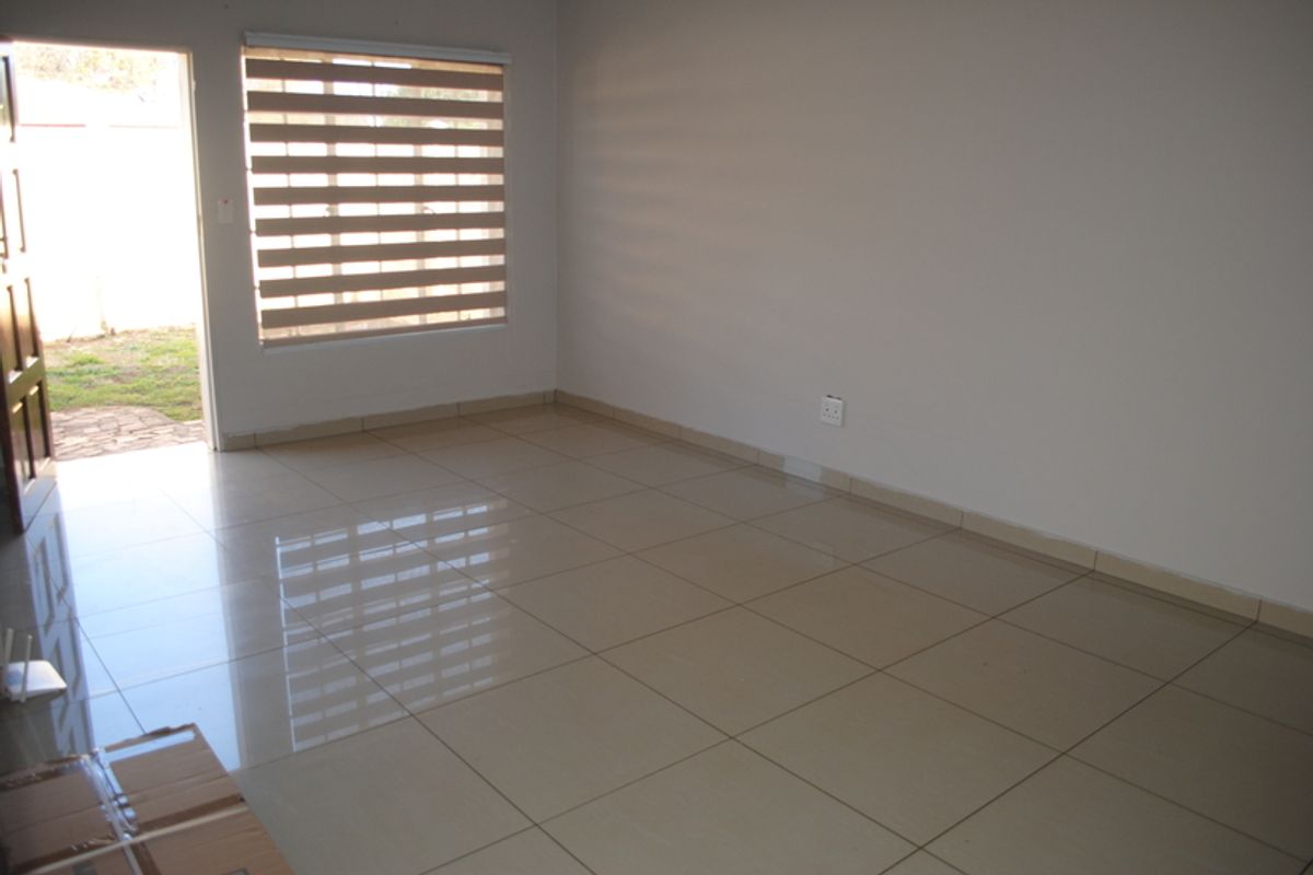A bright, empty living room featuring neutral tiled flooring, clean walls, and modern zebra blinds with direct access to the outdoor area.