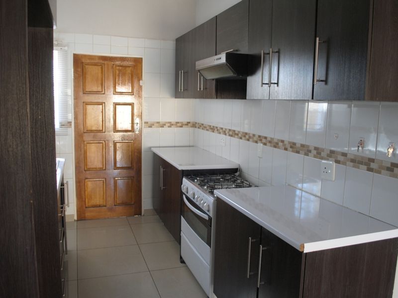 A functional kitchen featuring dark wood cabinetry, white tiled backsplash, gas stove with extractor fan, and tiled flooring.