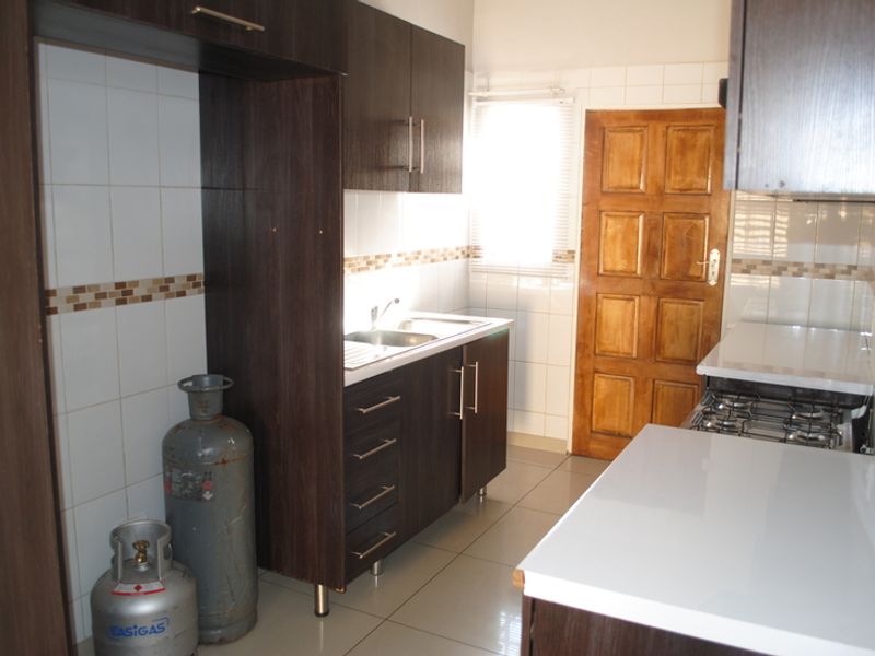 A functional kitchen featuring dark wood cabinetry, white tiled backsplash, stainless steel sink, and a built-in gas hob with tiled flooring.