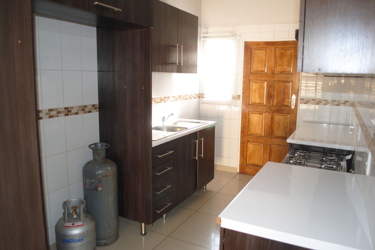 A functional kitchen featuring dark wood cabinetry, white tiled backsplash, stainless steel sink, and a built-in gas hob with tiled flooring.
