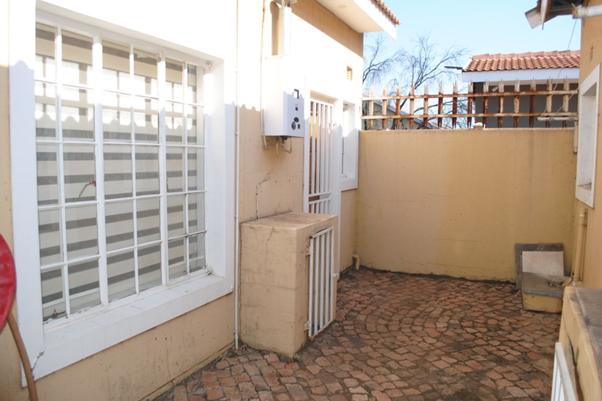 A rear courtyard area featuring paved flooring, a wall-mounted gas geyser, and perimeter walling with security spikes.