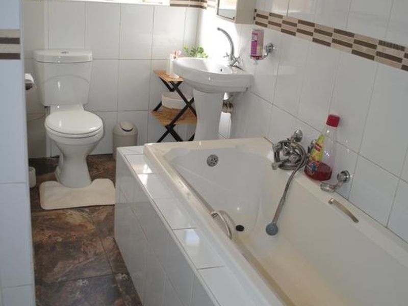 A functional bathroom featuring a pedestal basin, a built-in bathtub, and a toilet, finished with tiled walls and flooring.