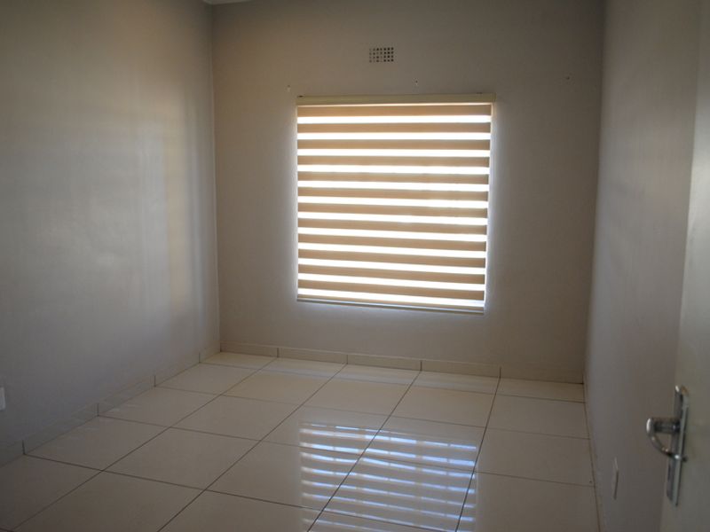 A clean, empty bedroom featuring neutral tiled flooring and modern zebra blinds, providing a blank canvas for personalization.
