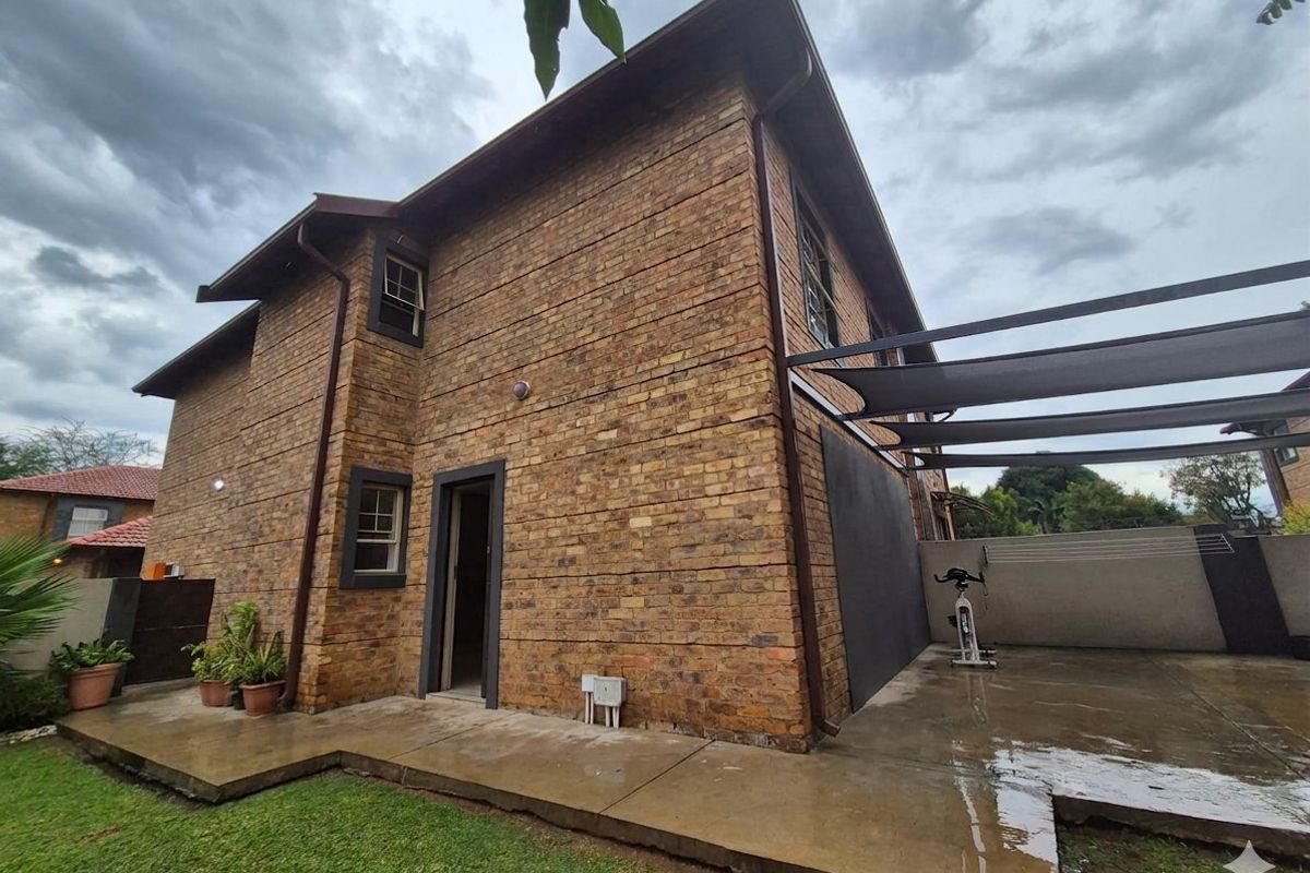 Rear view of the townhouse featuring face-brick exterior, a paved patio area with shade sail, and a small private garden.