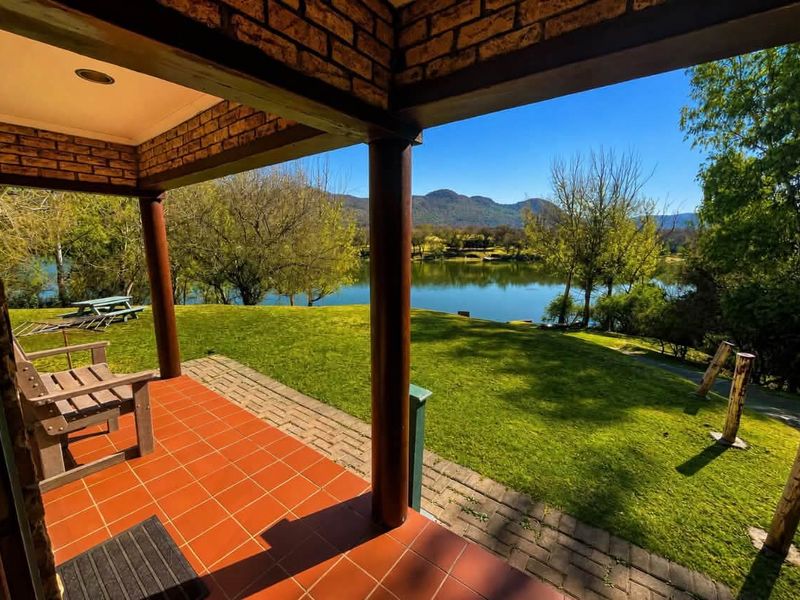 Covered patio featuring terracotta tiling and brick pillars, offering scenic views over the garden and lake.
