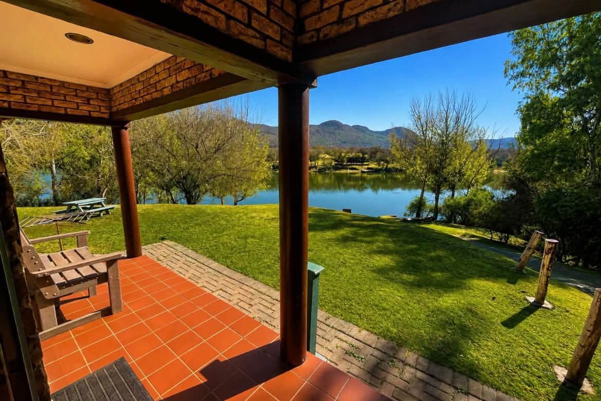 Covered patio featuring terracotta tiling and brick pillars, offering scenic views over the garden and lake.