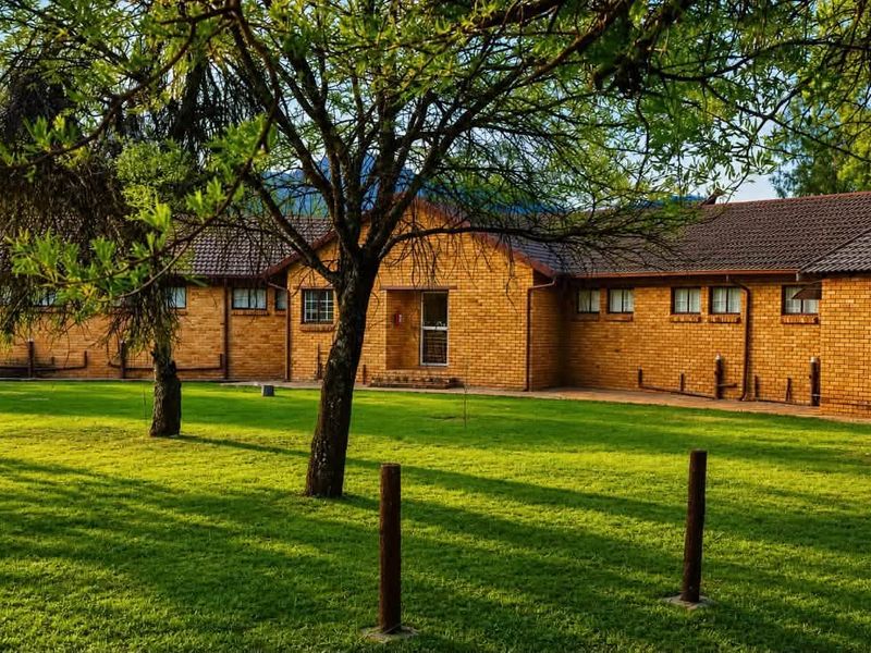 A well-maintained face-brick exterior of a small holding property, featuring a spacious lawn, mature trees, and a tiled roof.