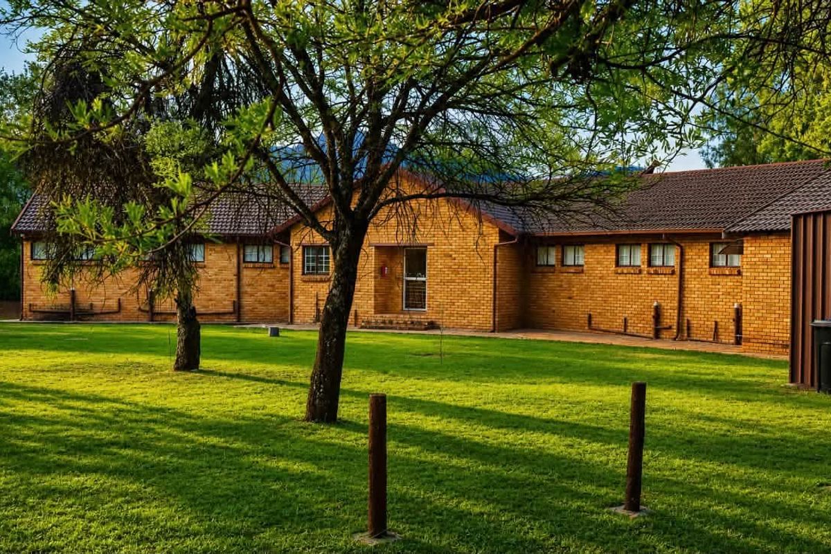 A well-maintained face-brick exterior of a small holding property, featuring a spacious lawn, mature trees, and a tiled roof.