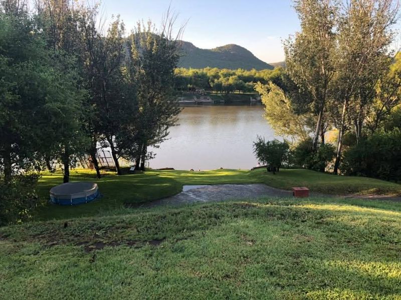 Scenic view overlooking a tranquil river with expansive green lawns and mature trees, offering a peaceful outdoor setting.