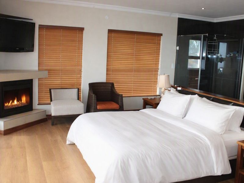 Spacious bedroom featuring laminate flooring, a built-in fireplace, timber blinds, and an integrated en-suite bathroom with a modern glass shower enclosure.