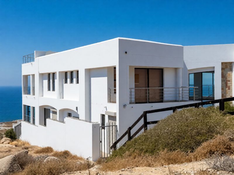 Modern multi-level coastal residence featuring white rendered facade, stainless steel balcony railings, and expansive ocean views.