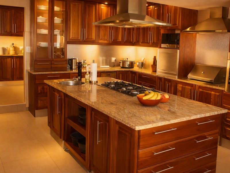 Spacious kitchen featuring rich wooden cabinetry, granite countertops, a central island with a gas hob, and integrated stainless steel appliances.