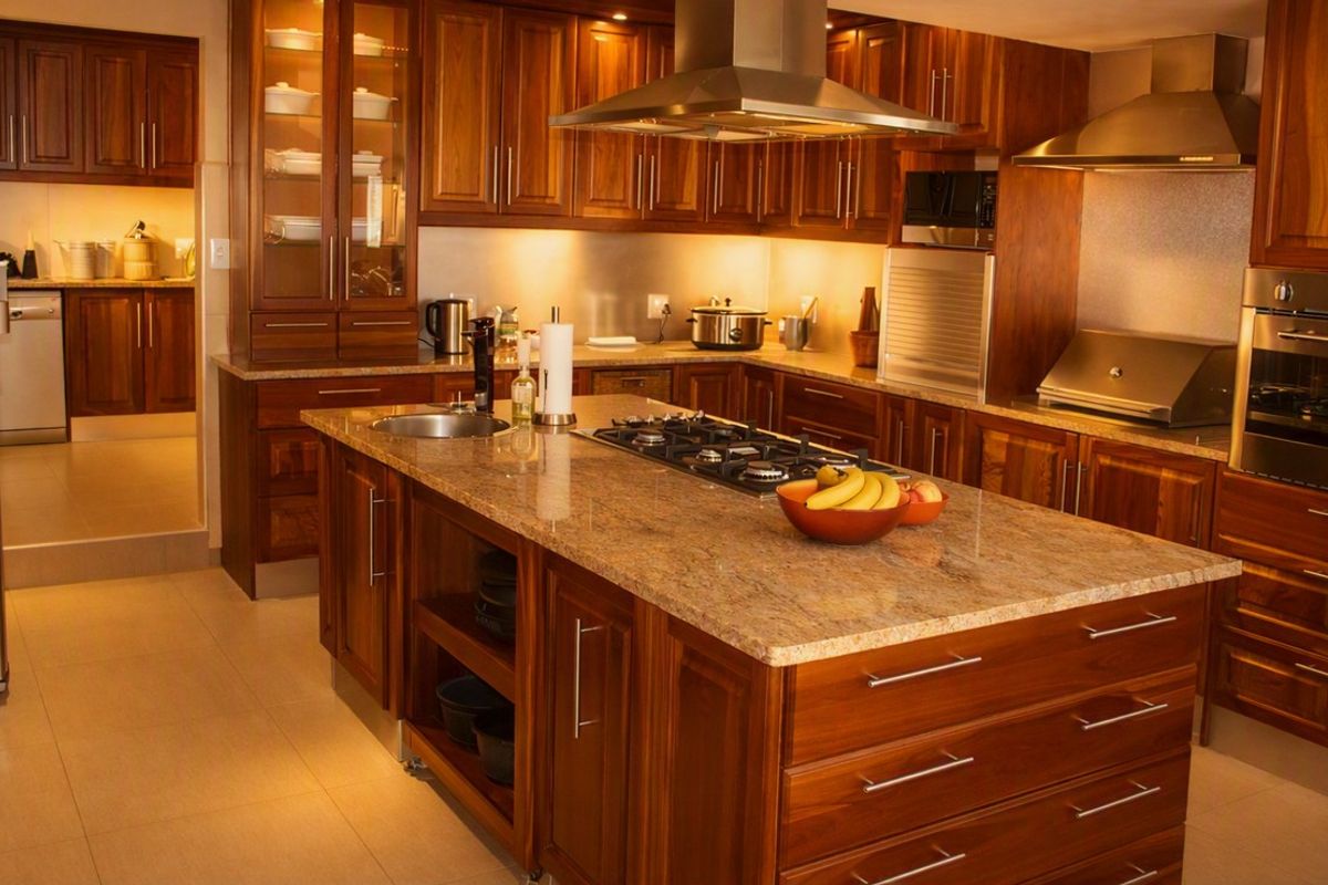 Spacious kitchen featuring rich wooden cabinetry, granite countertops, a central island with a gas hob, and integrated stainless steel appliances.