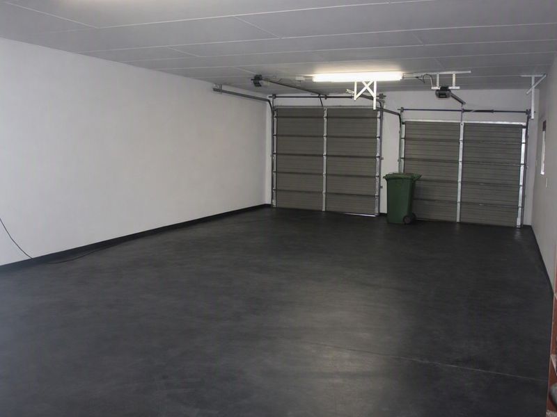 A spacious, clean double garage featuring painted concrete flooring, automated garage doors, and functional overhead lighting.
