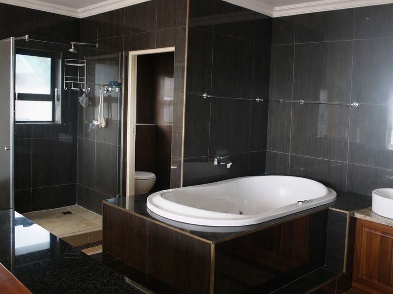Modern bathroom featuring dark tiled walls, a built-in bathtub, a vessel sink with granite vanity, and a separate glass-enclosed shower area.