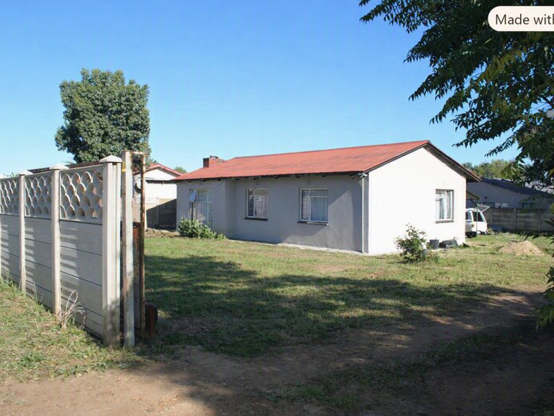 Rear view of a detached house featuring a corrugated metal roof, plastered exterior walls, and a precast concrete boundary wall set on a large plot.