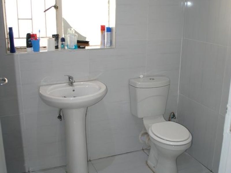 A functional bathroom featuring a pedestal basin, toilet, and fully tiled surfaces, requiring minor repairs to the window.