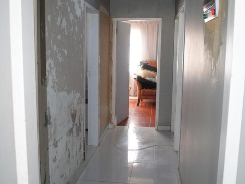 A hallway featuring tiled flooring and a ceiling with coving, currently requiring significant wall repairs and cosmetic refurbishment.