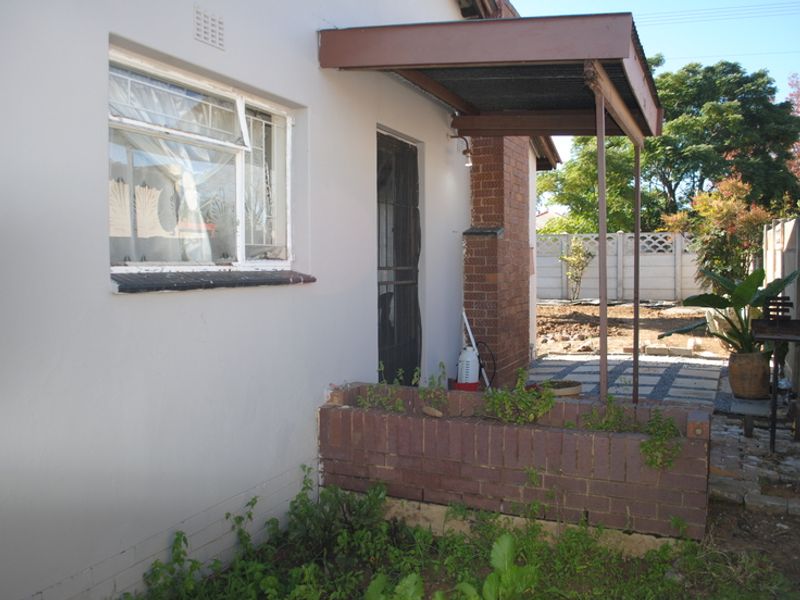 Rear exterior view showing a small covered patio area, brick planter box, and precast concrete boundary walling.