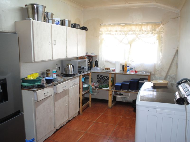 A dated kitchen area featuring built-in cabinetry and tiled flooring, currently showing significant signs of wear and wall damage requiring maintenance.