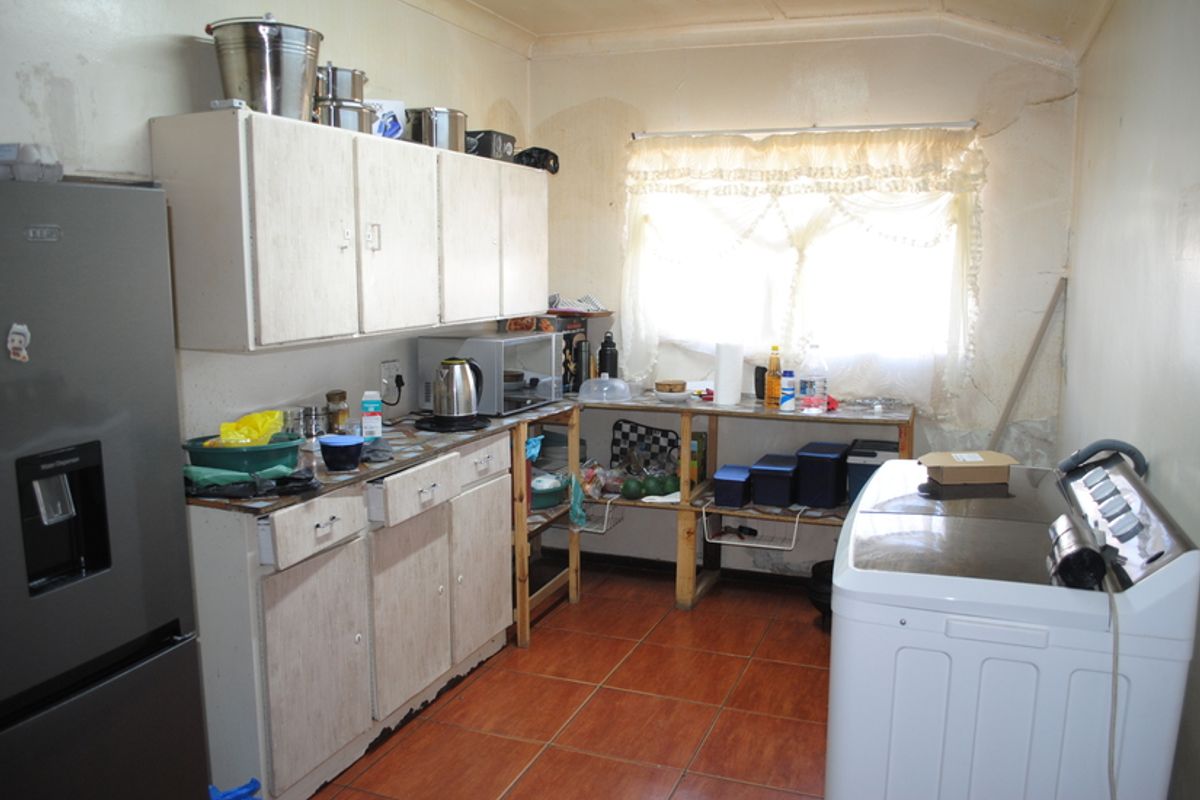 A dated kitchen area featuring built-in cabinetry and tiled flooring, currently showing significant signs of wear and wall damage requiring maintenance.