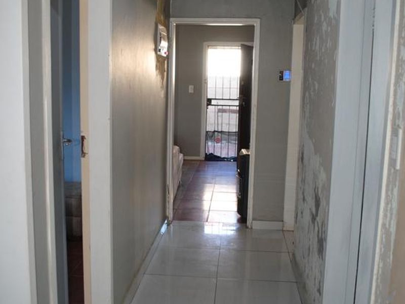 A vacant hallway featuring tiled flooring and recessed lighting, currently requiring wall repairs and cosmetic finishing to restore its condition.