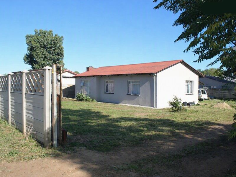 A detached house featuring a corrugated metal roof and a large surrounding garden enclosed by a precast concrete boundary wall.