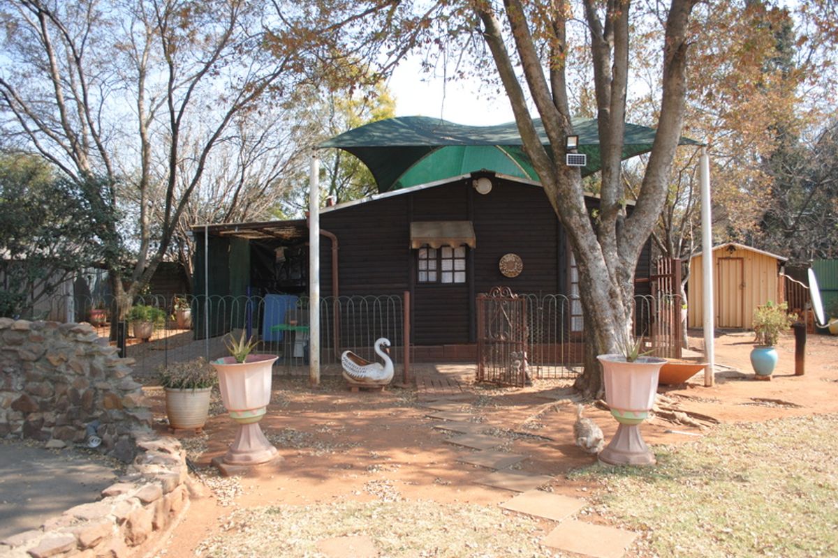Rear view of a timber-clad dwelling featuring a shade sail, metal fencing, and a stone retaining wall set within a natural garden landscape.