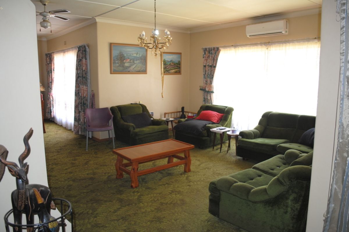 A spacious living room featuring carpeted flooring, a ceiling fan, a chandelier, and a wall-mounted split-system air conditioner.