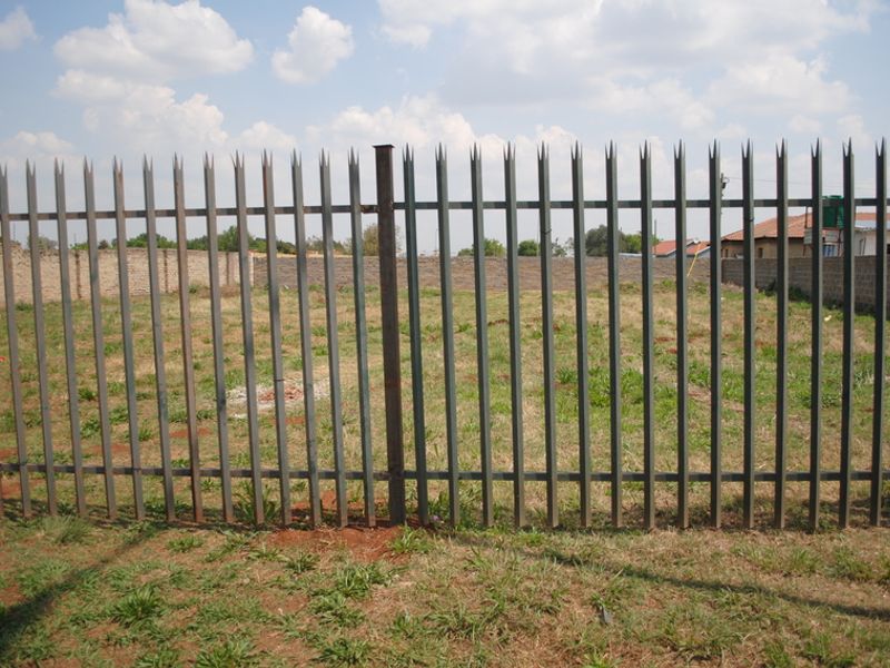 A vacant residential plot secured with steel palisade fencing and perimeter brick walls, offering a clear space for future development.
