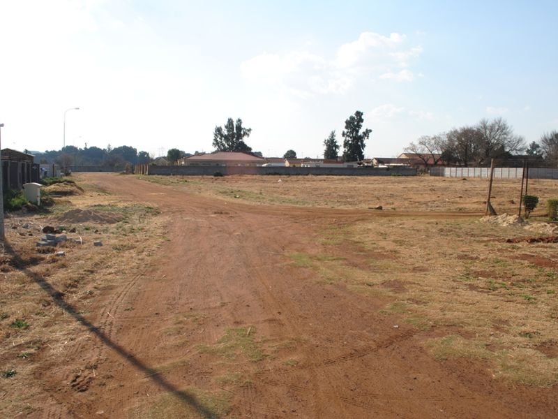 A view of a vacant residential plot featuring a dirt road and perimeter walling in a suburban setting.